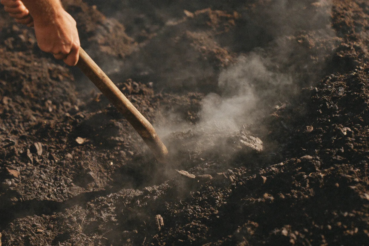 Weathered hands turning a steaming pile of compost with a pitchfork